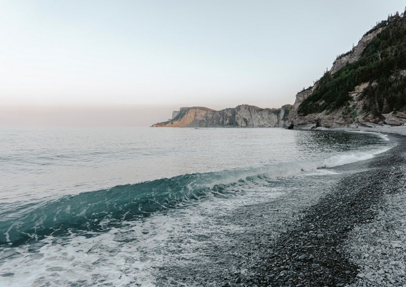 Coastal cliffs and a breaking teal wave on a pebble beach at dusk