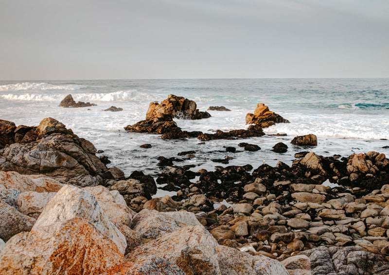 Rocky coastline with rust-coloured lichen, breaking waves and a pale overcast sky