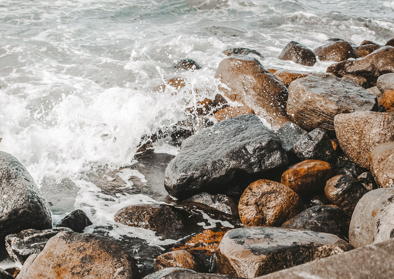 Close-up of ocean waves breaking over grey, tan and rust-toned rocks