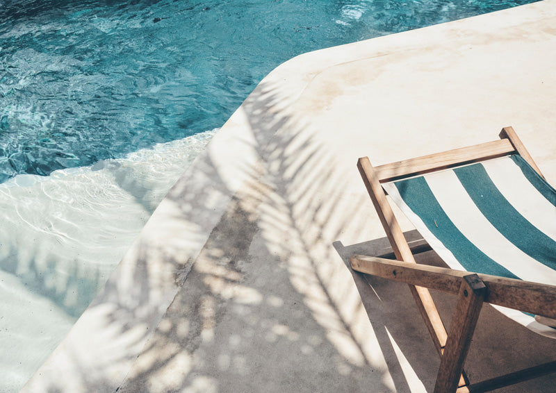 Overhead view of pool corner with striped deckchair and palm frond shadow