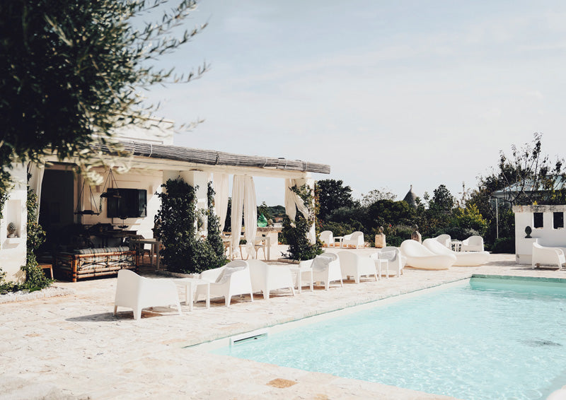 Poolside terrace with white lounge chairs, teal pool water and cream stone paving under a pergola