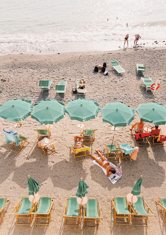 Aerial view of teal beach umbrellas, chairs and sunbathers on sand beside the ocean