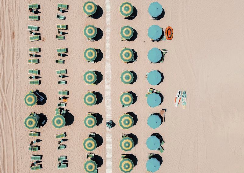 Aerial view of beach umbrellas and sun loungers in rows on sand with surfboards