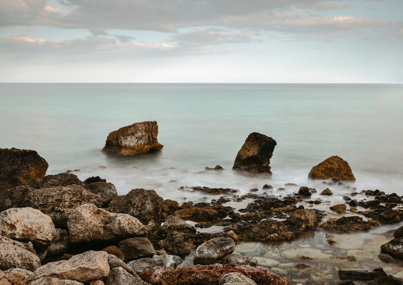 Rocky shoreline with scattered boulders and a misty, calm sea under an overcast sky