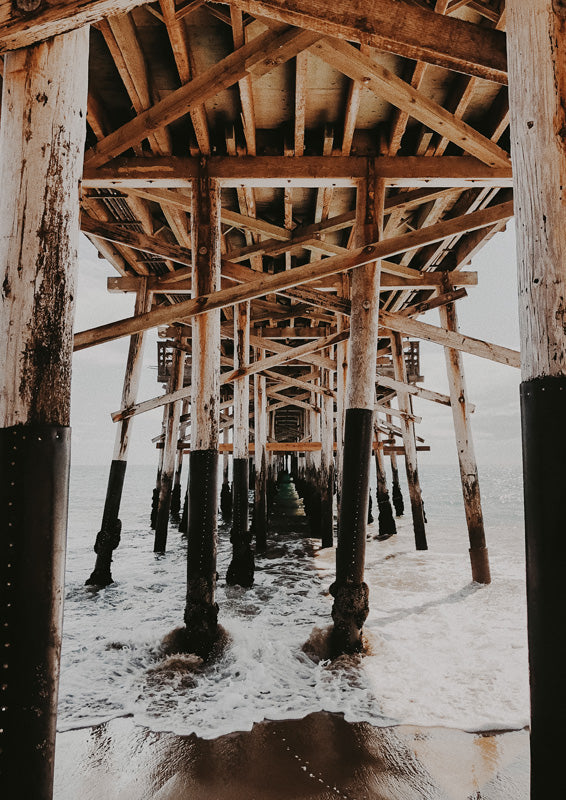 View beneath a weathered wooden pier looking out toward the ocean and breaking waves
