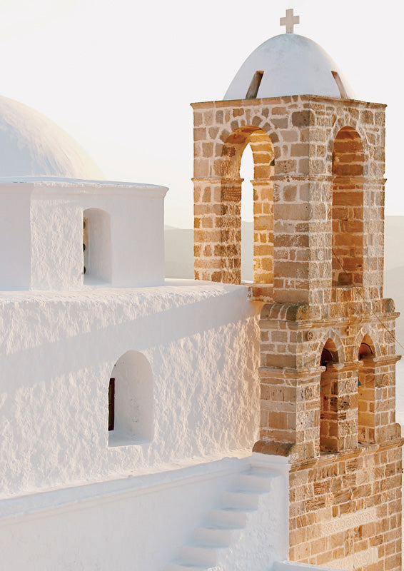 Whitewashed chapel dome and terracotta stone bell tower with arched openings against a pale sky