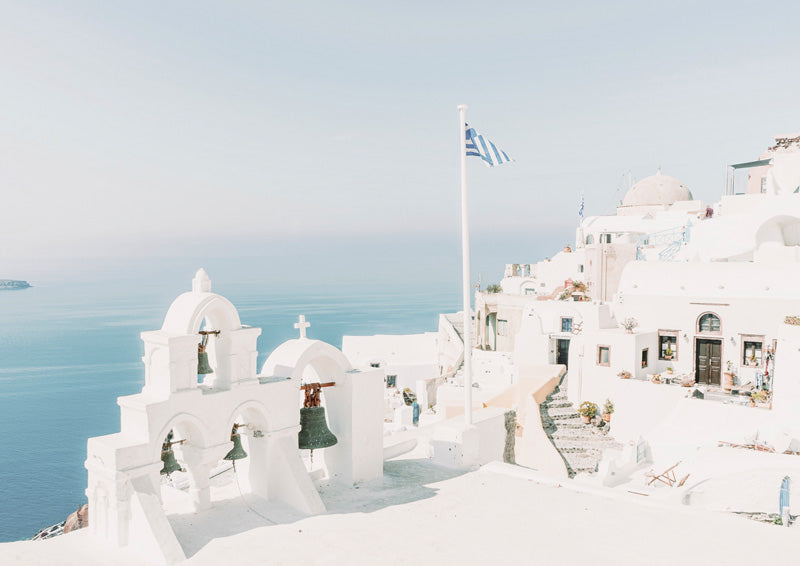 Whitewashed Santorini bell towers and flag overlooking the sea