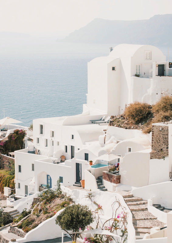 Whitewashed Santorini-style buildings on a cliff above the sea with a small pool and bougainvillea