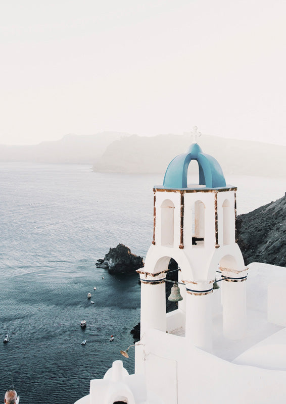 White bell tower with blue dome overlooking the sea and boats at Santorini