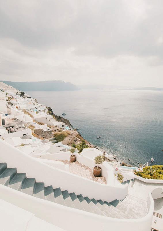 Whitewashed staircase and cliffside buildings overlooking a calm blue bay under a hazy sky