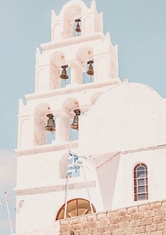 Whitewashed Santorini bell tower with bronze bells against a pale blue sky