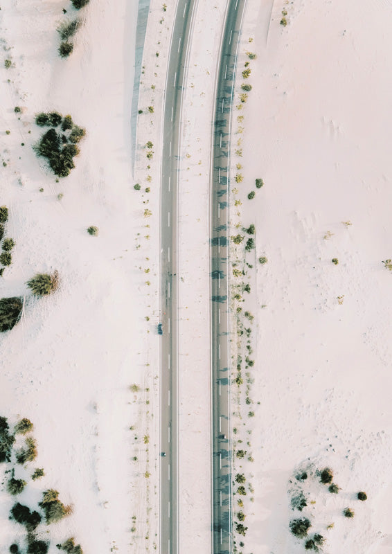 Aerial photo of a winding desert road through pale sand with scattered sage shrubs