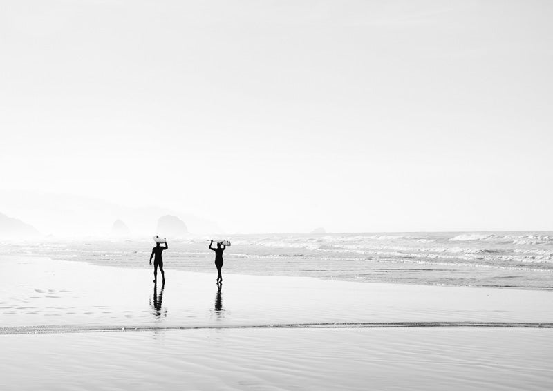 Black and white photo of two surfers carrying boards along a foggy beach