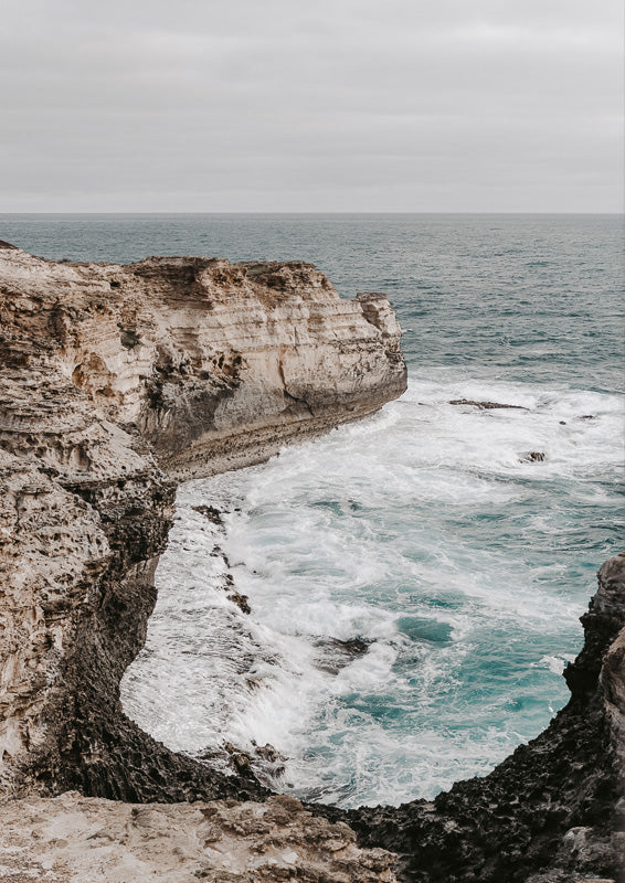 Photograph of layered coastal cliffs and turquoise ocean waves under an overcast sky