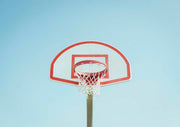 Low angle photo of a red and white basketball hoop against a pale blue sky