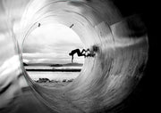 Silhouetted skateboarder inside a round tunnel with ocean horizon visible through the opening