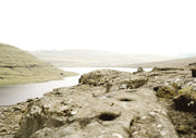 Rocky foreshore beside a calm lake with hills and pale sky in the distance