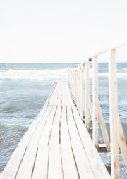Weathered wooden boardwalk with railing leading to ocean waves under a pale sky