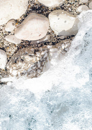 Overhead close-up of pale shoreline rocks with white sea foam washing over them