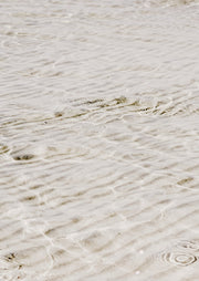 Close-up photograph of sand ripples under shallow clear water in beige tones