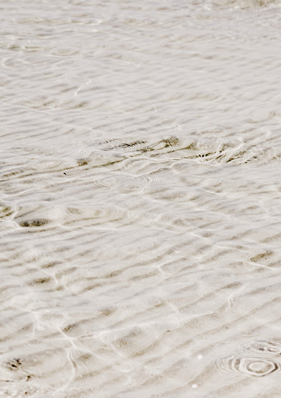 Close-up photograph of sand ripples under shallow clear water in beige tones