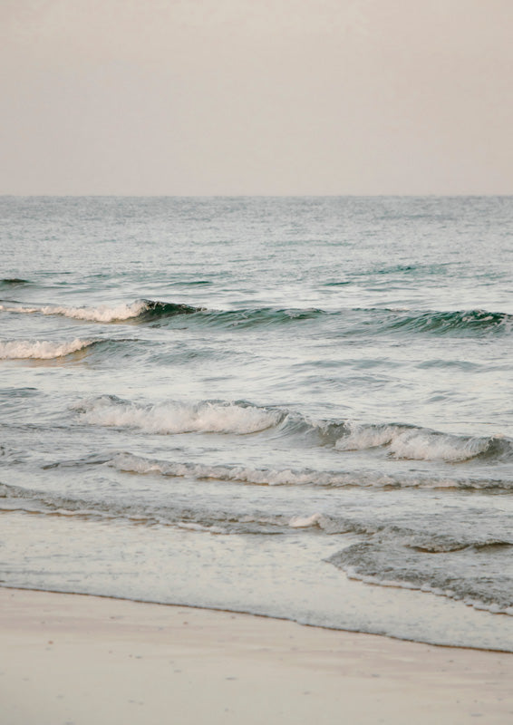 Gentle ocean waves breaking on a sandy beach under a muted pale sky