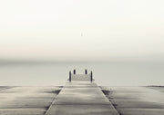 Foggy monochrome photograph of an empty pier leading to a still horizon with a seagull overhead