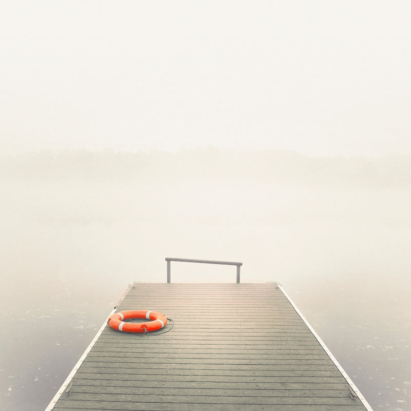 Orange lifebuoy on a wooden pier extending into fog-covered water with a faint treeline