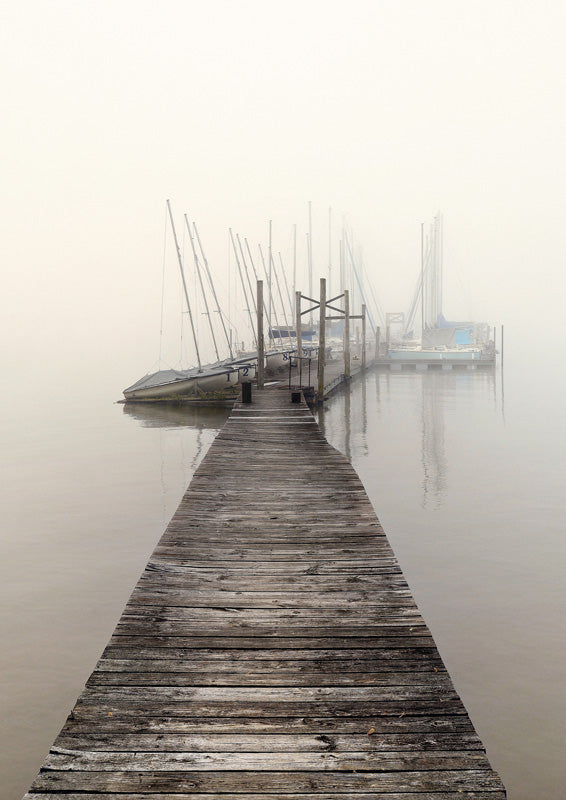 Weathered wooden pier leading to moored sailboats in thick harbor fog
