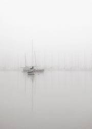 Black and white photo of sailboats moored in a foggy harbour with still reflective water
