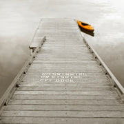 Sepia photograph of a wooden dock with warning text and an orange kayak on misty water
