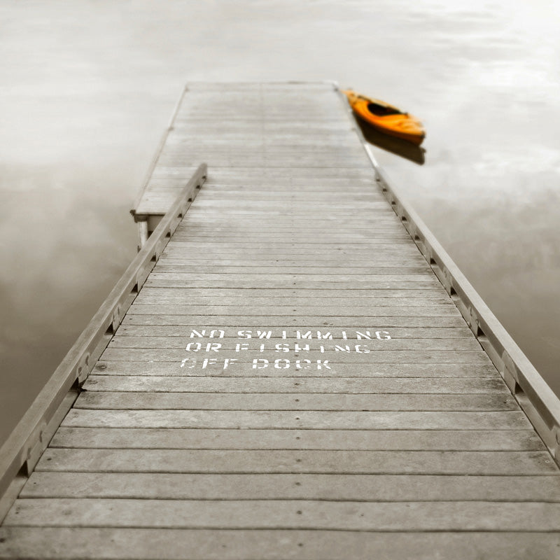 Sepia photograph of a wooden dock with warning text and an orange kayak on misty water