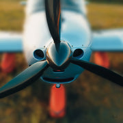 Close-up front view of an aircraft nose, three-blade propeller and orange landing gear.