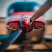 Close-up of a red airplane propeller spinner with blades crossing in front of a blurred fuselage