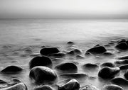 Black and white long exposure photo of dark boulders in misty coastal water
