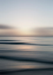 Blurred seascape photograph with soft waves and a glowing pink and blue horizon at dusk