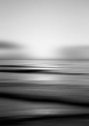 Black and white long-exposure photograph of a calm sea with a blurred horizon and soft light reflection