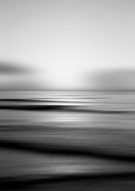 Black and white long-exposure photograph of a calm sea with a blurred horizon and soft light reflection