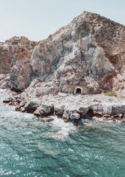 Rocky limestone cliff with a stone archway ruin above turquoise sea water