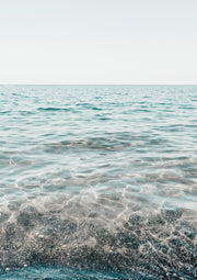 Clear turquoise water over pale sand with a soft horizon line and pale sky