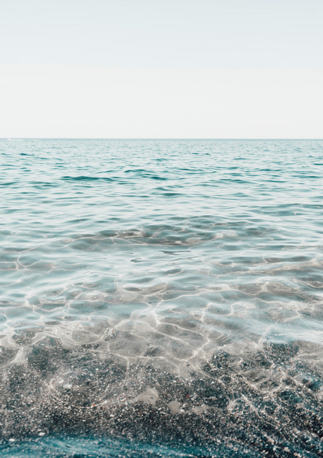 Clear turquoise water over pale sand with a soft horizon line and pale sky