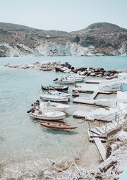 Small boats moored at a white stone quay beside turquoise water and rocky hills