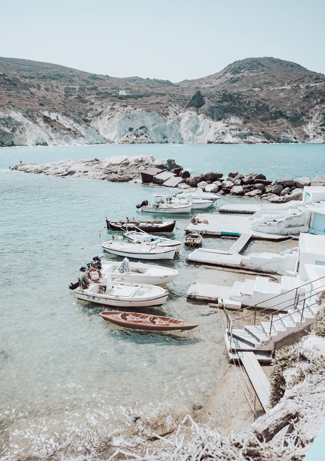 Small boats moored at a white stone quay beside turquoise water and rocky hills