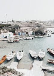 Small boats moored in a pale turquoise harbour with whitewashed buildings and rocky hills