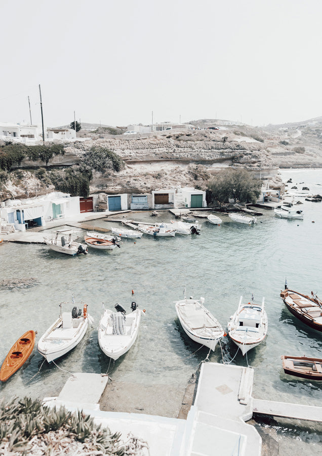 Small boats moored in a pale turquoise harbour with whitewashed buildings and rocky hills