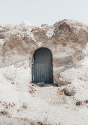 Weathered blue-grey door set into a rough, chalky rock archway under a pale sky