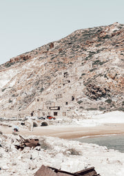 Abandoned stone building on a rocky hillside above a sandy beach and calm sea